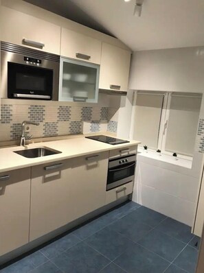 Modern kitchen with double sink, oven, and microwave, featuring a window and neutral-toned cabinetry.