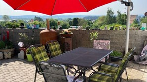 An outdoor patio with a table and chairs under a red umbrella, surrounded by potted plants and a stone wall. - Spacious, first floor vacation apartment in the Allgäu  (Memmingen)