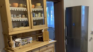 A kitchen with a wooden cabinet containing dishes and a refrigerator. - Spacious, first floor vacation apartment in the Allgäu  (Memmingen)