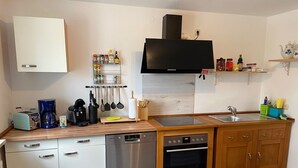 A compact kitchen with a dishwasher, oven, and a flat-screen TV mounted above the counter. - Spacious, first floor vacation apartment in the Allgäu  (Memmingen)