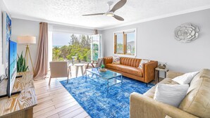 A modern living room with a glass coffee table, leather sofa, and a ceiling fan. - Gertrude's Siesta | Oceanview, 12 Steps to Beach, 4min Trolley to Village, Free Gear (Siesta Key)