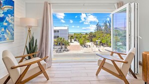 A balcony with two wooden chairs, a floor lamp, and a painting on the wall. - Gertrude's Siesta | Oceanview, 12 Steps to Beach, 4min Trolley to Village, Free Gear (Siesta Key)