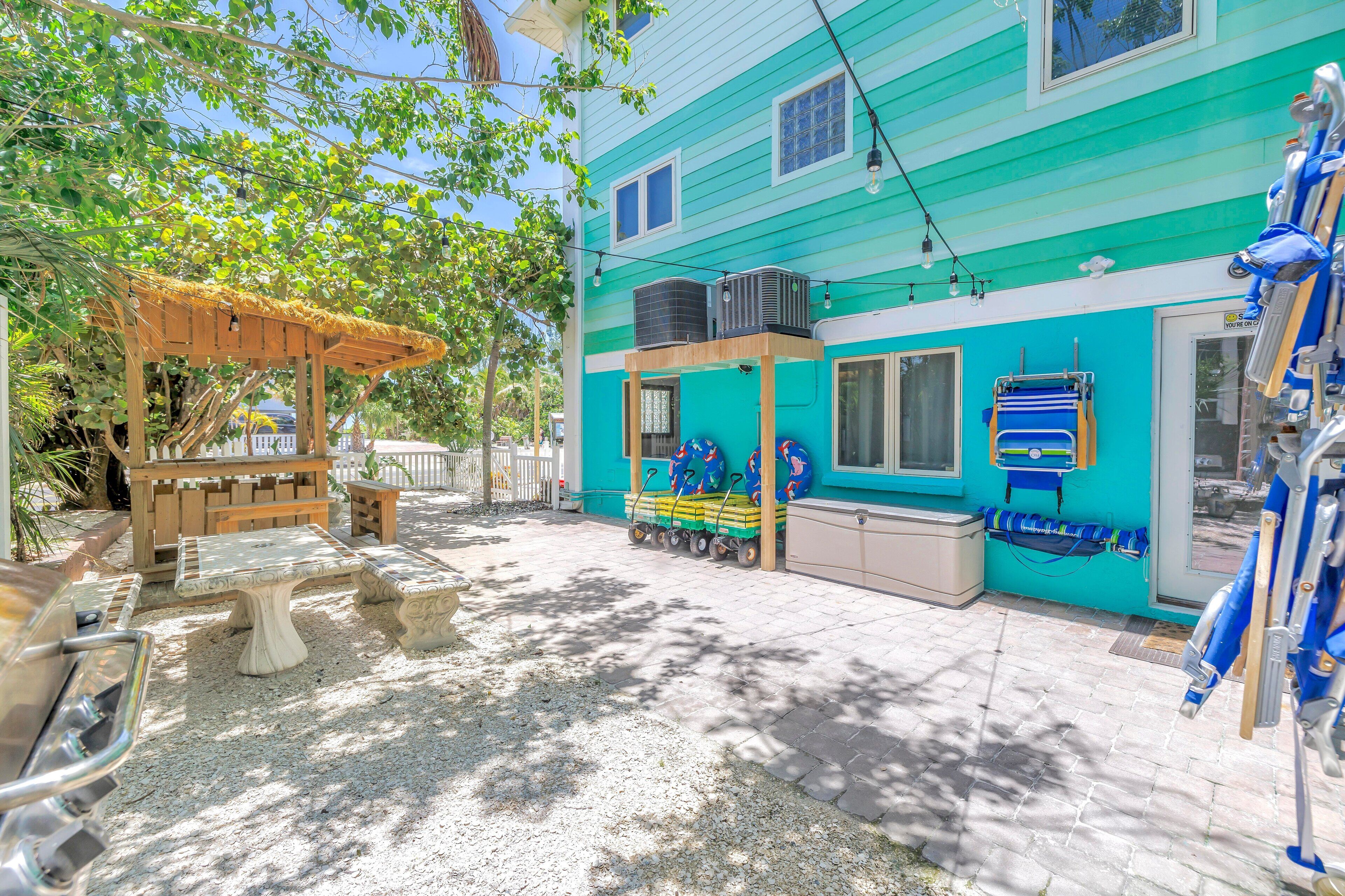 A turquoise house with a patio area featuring a wooden pergola, a play area with a slide, and a pool table.