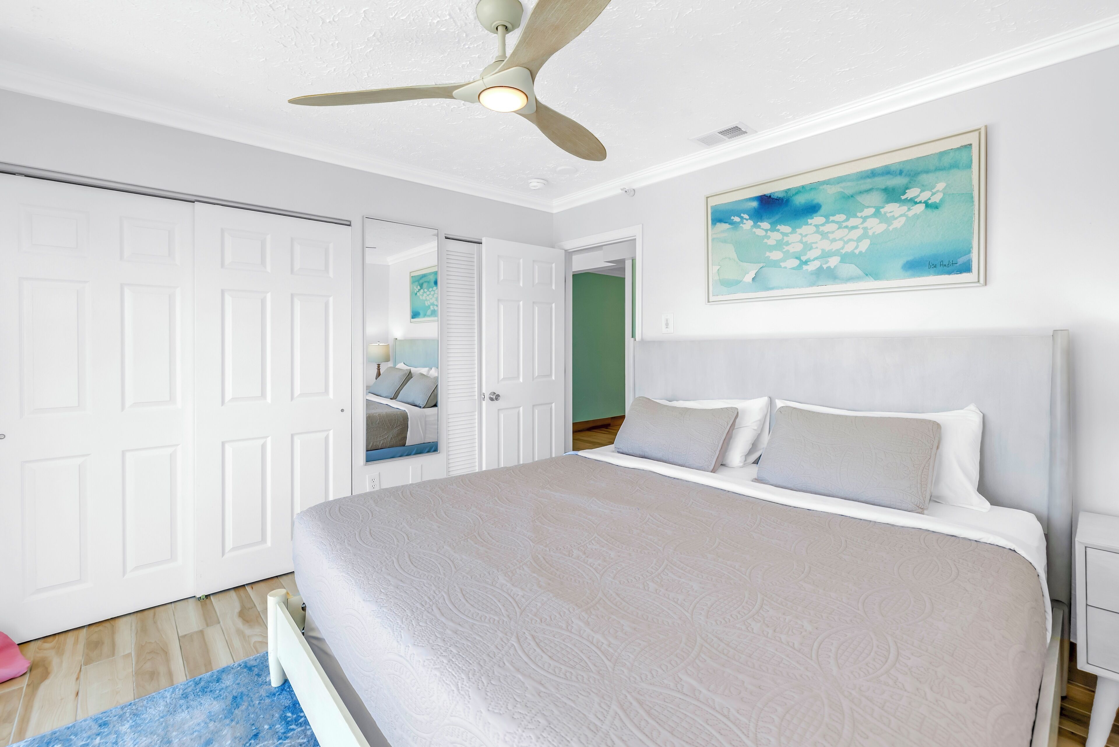 A bedroom with a bed, a ceiling fan, a door, and a painting on the wall.