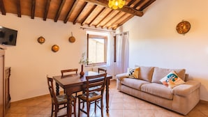 A dining area with a wooden table and chairs, a sofa, and a window with curtains. - Leondardo Apartment ~ LE FRAINE (New Opening 2022) (Santa Luce)