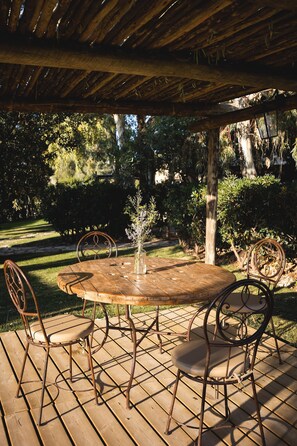 An outdoor wooden deck with a round table and metal chairs, surrounded by lush greenery. - Leondardo Apartment ~ LE FRAINE (New Opening 2022) (Santa Luce)