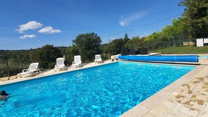 Une piscine rectangulaire à l’eau d’un bleu cristallin, entourée de chaises longues blanches et d’une clôture verte.