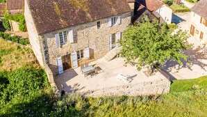 Une maison en pierre avec un toit en tuiles, une terrasse dallée et un jardin.
