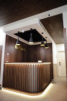 Un mostrador de recepción con detalles de madera y un letrero que dice "ROOTTOP". Tres lámparas colgantes iluminan el área sobre el mostrador.