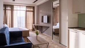 A modern hotel room with a sofa, a small table with a vase, a bed, a desk, and a TV mounted on the wall. - Rooftop Apart Hotel (Yerevan)