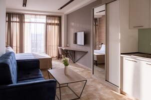 Una habitación de hotel moderna con sofá, una mesita con un florero, cama, escritorio y televisor montado en la pared.