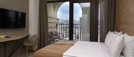 A hotel room with a bed, a desk with a television, a chair, and a balcony with a city view.