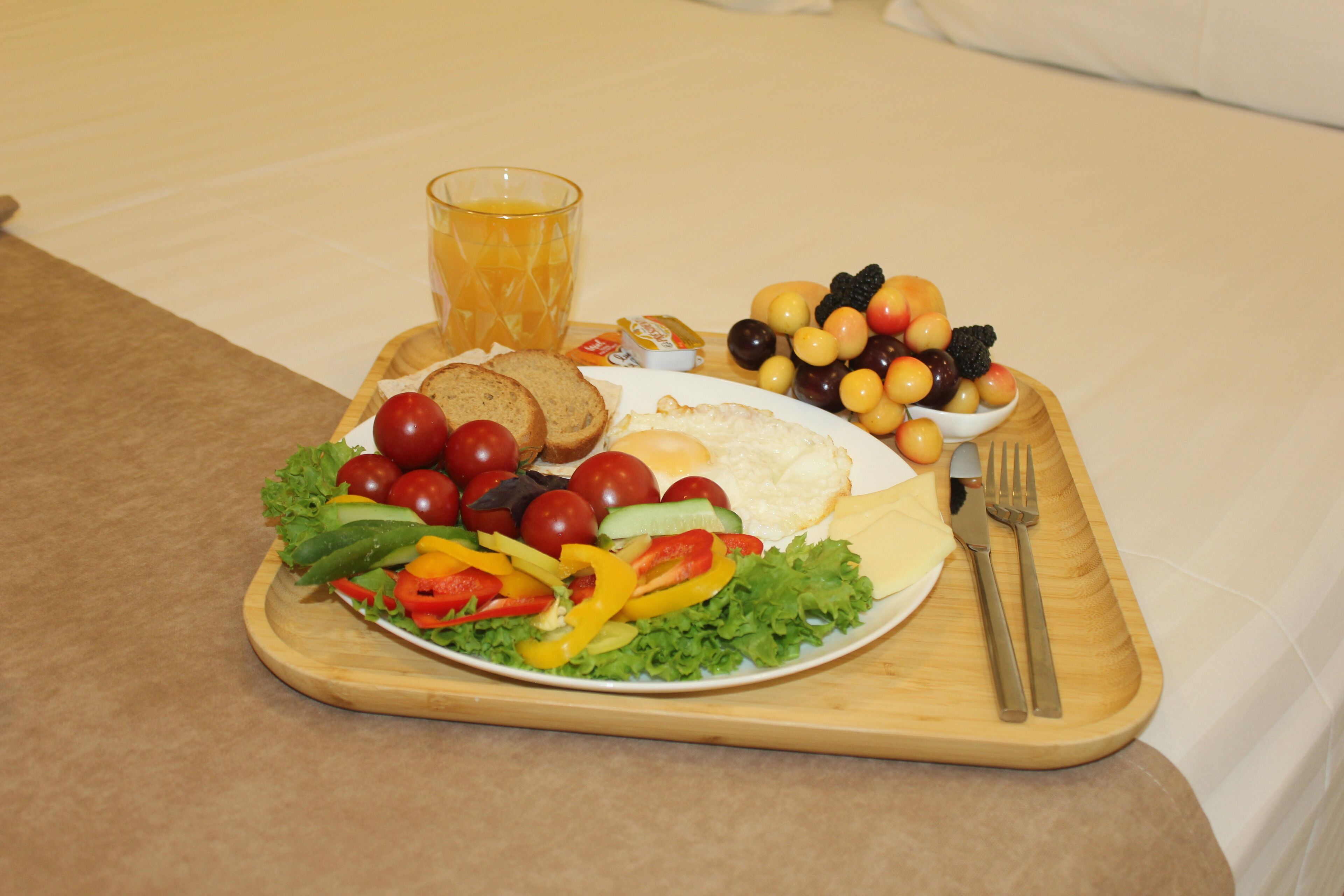 A breakfast tray with a variety of foods including eggs, toast, a salad, and a glass of orange juice.
