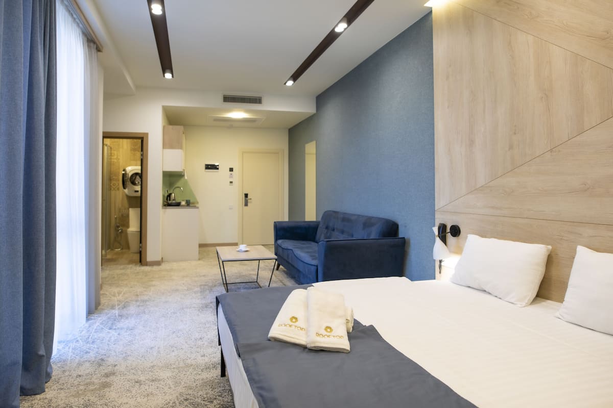 A hotel room with a bed, a chair, a desk, and a bathroom visible through an open door.