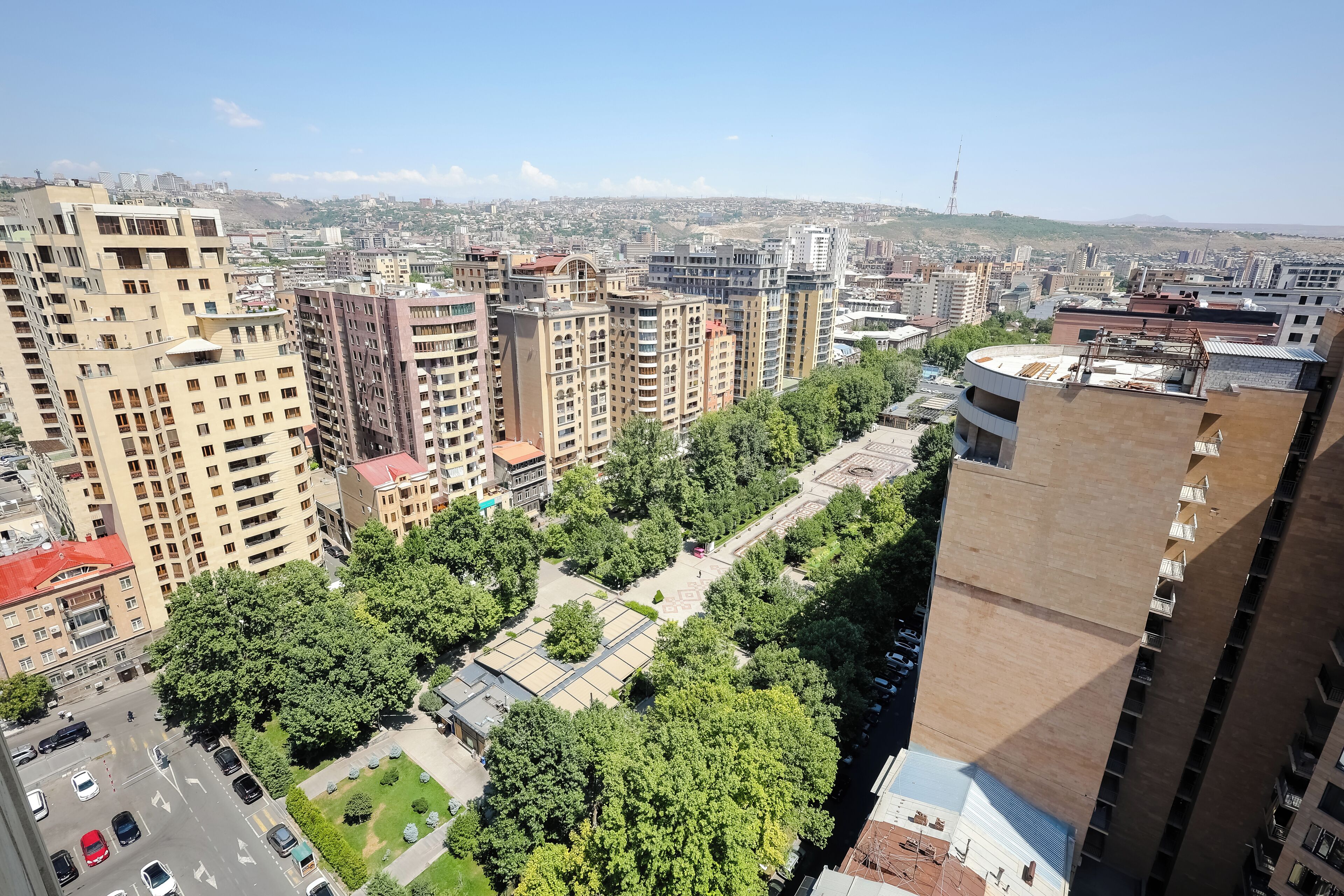 Un edificio alto con varios pisos, rodeado de vegetación y otros edificios.