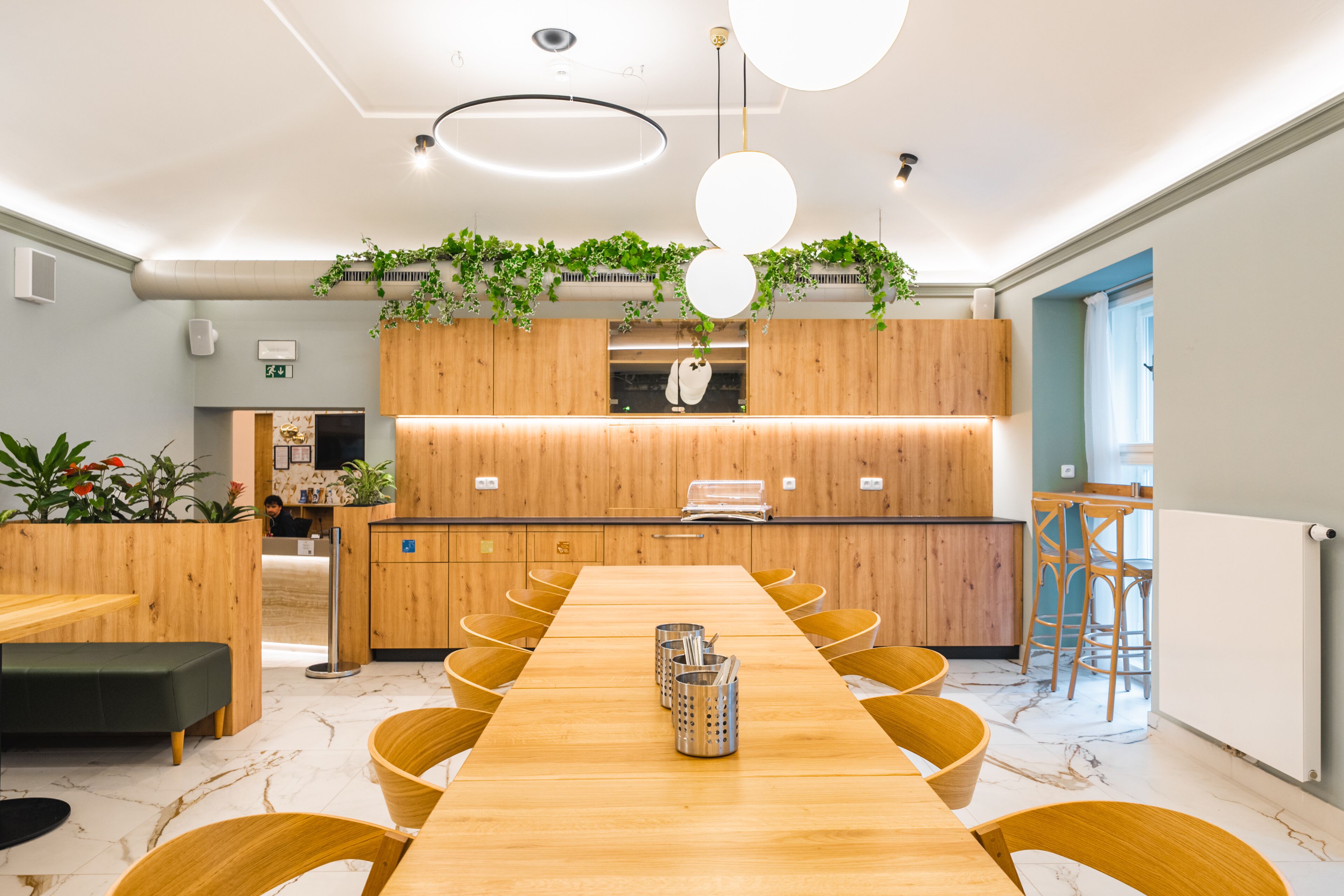 A modern dining area with a long wooden table, yellow chairs, and a kitchen in the background.