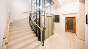 A modern hotel lobby with a glass elevator, a wooden door, and a staircase with a metal railing. - LUMA TERRA PRAGUE (Prague)