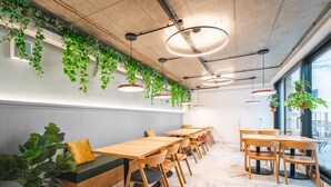 A modern dining area with wooden tables and chairs, green plants hanging from the ceiling, and a view of the city through large windows. - LUMA TERRA PRAGUE (Prague)