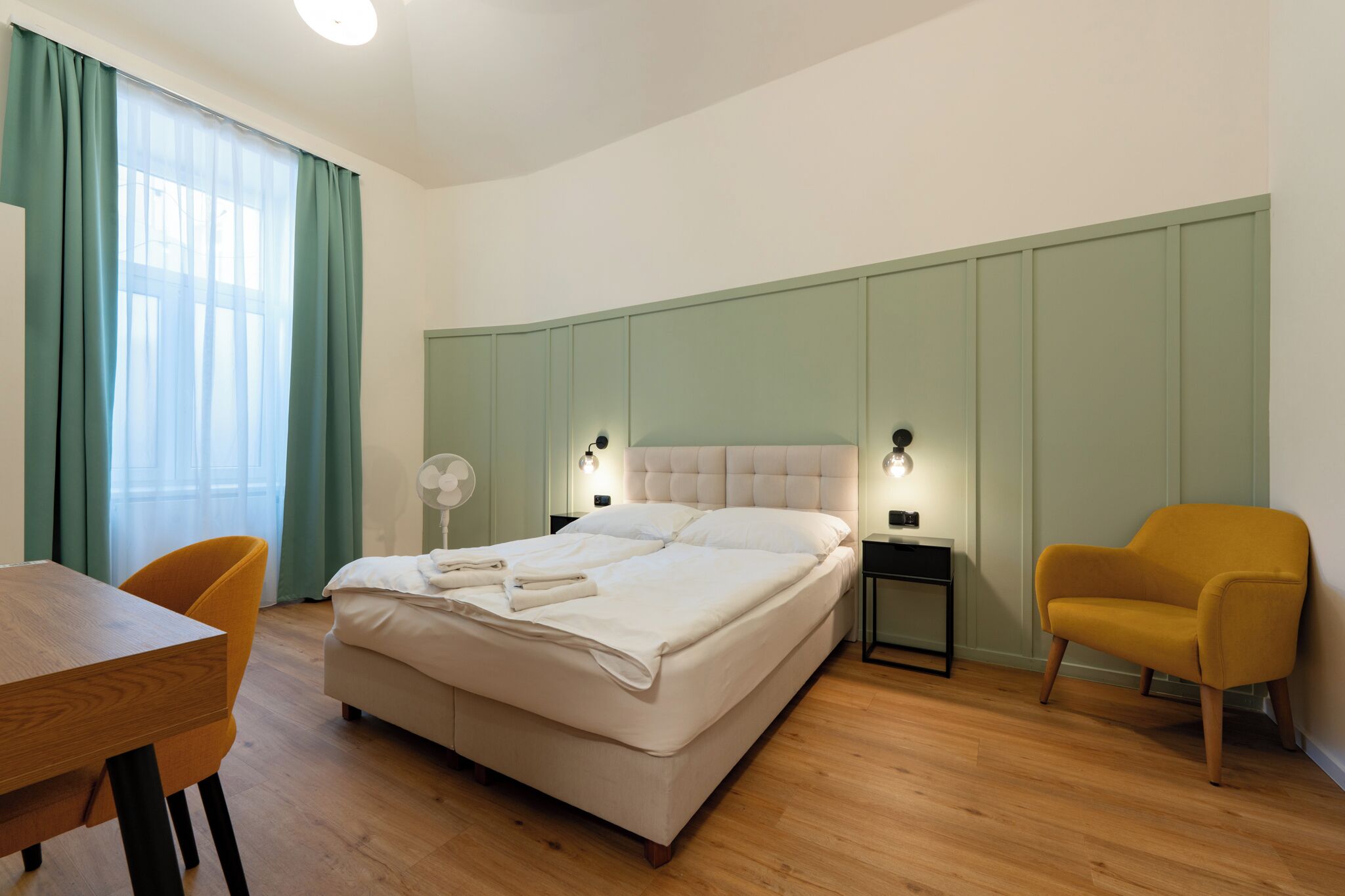 Un dormitorio con cama, escritorio, silla y mesita de noche con lámpara.