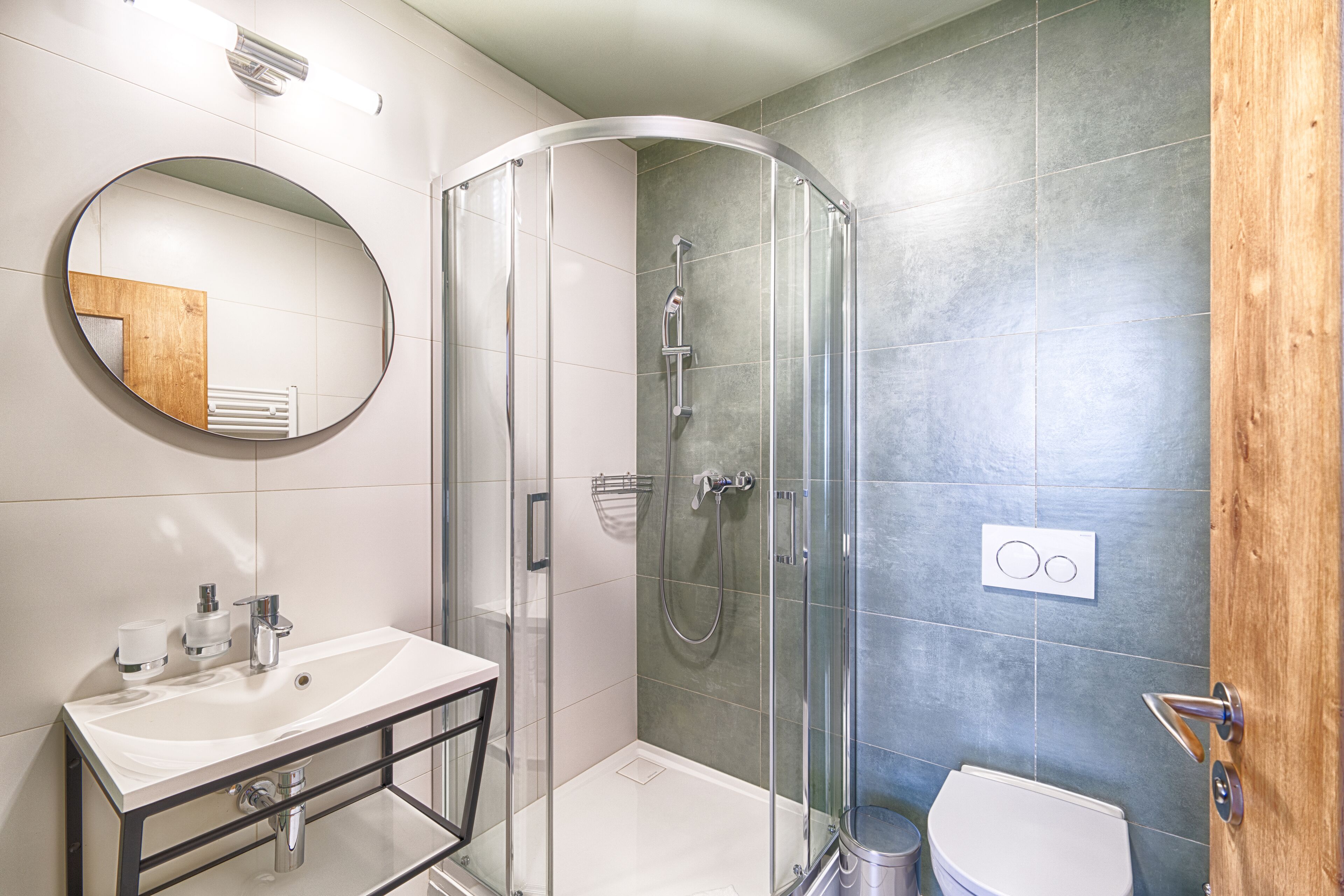 Un bagno moderno con doccia vetrata, specchio tondo e lavandino bianco.