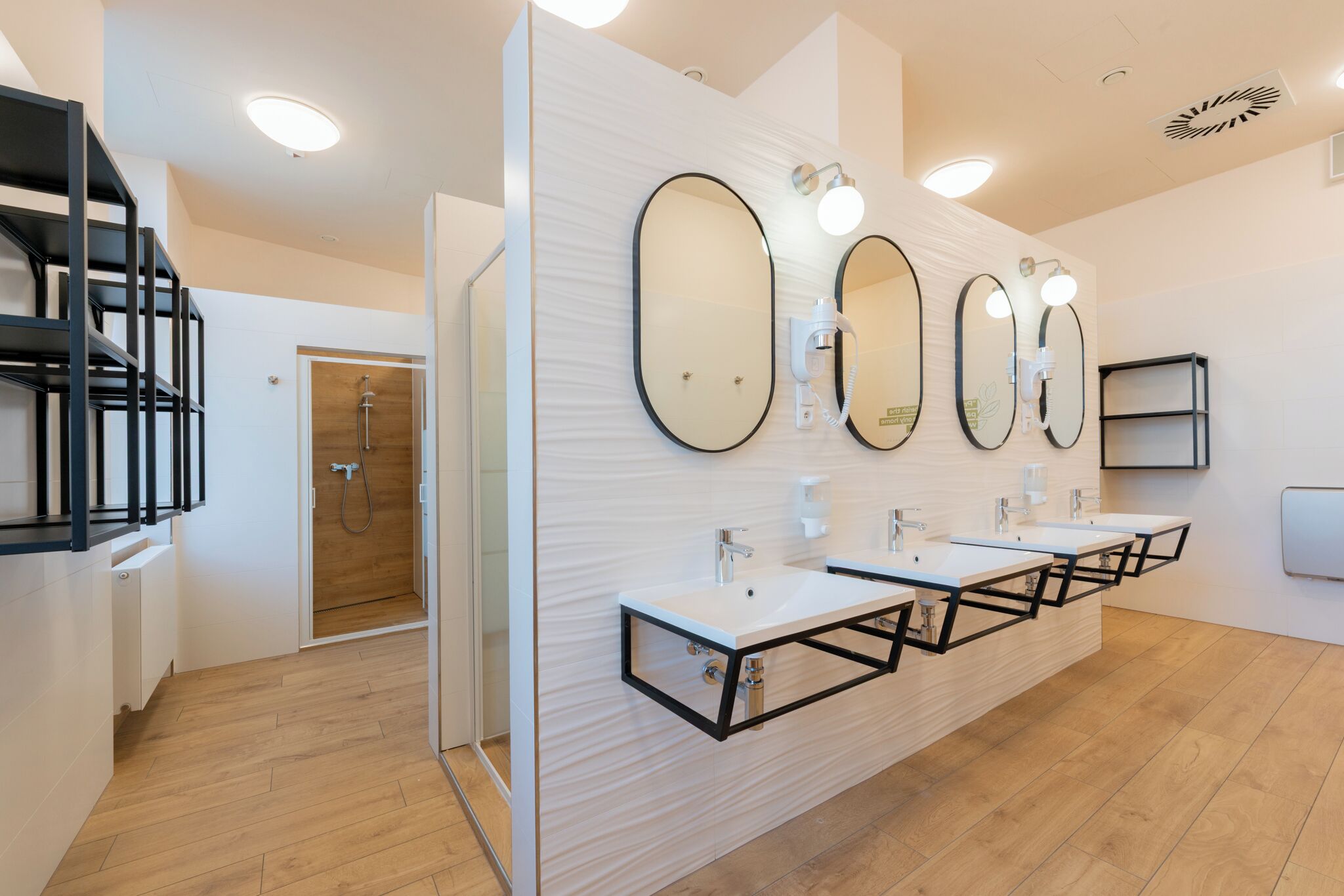 A modern bathroom with three sinks, large mirrors, and a shower.