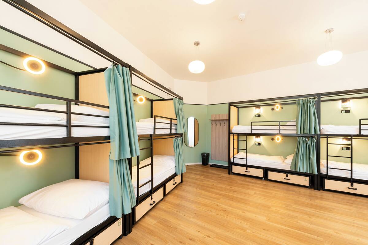 A dormitory room with bunk beds, wooden floors, and wall-mounted lights.