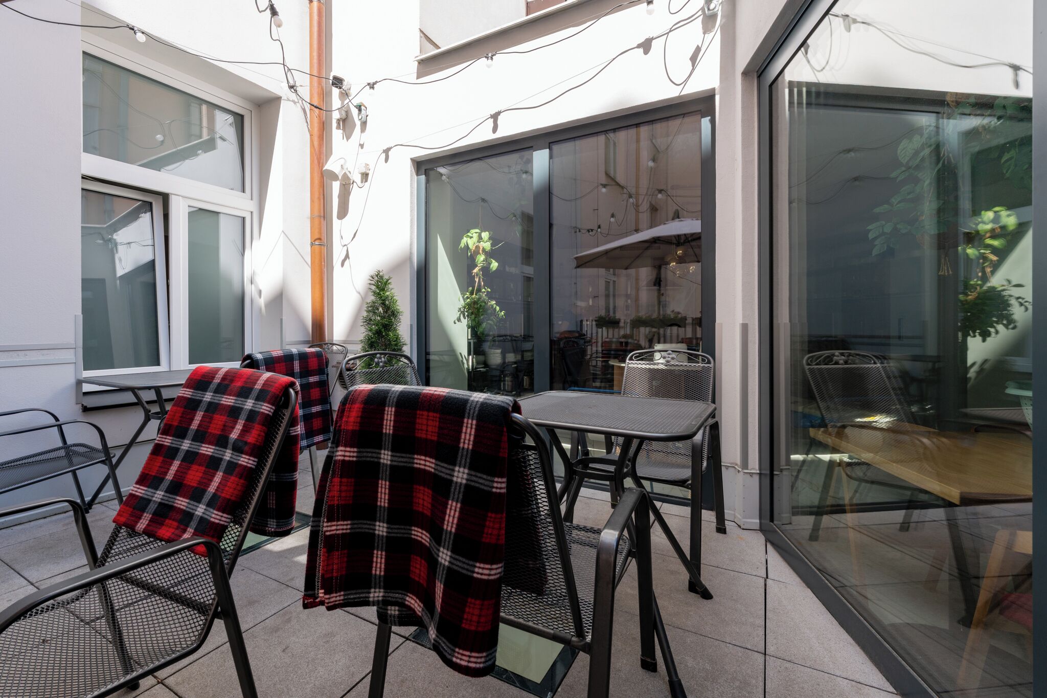 An outdoor patio with metal chairs and tables, some covered with plaid blankets, and a view of a restaurant through glass doors.