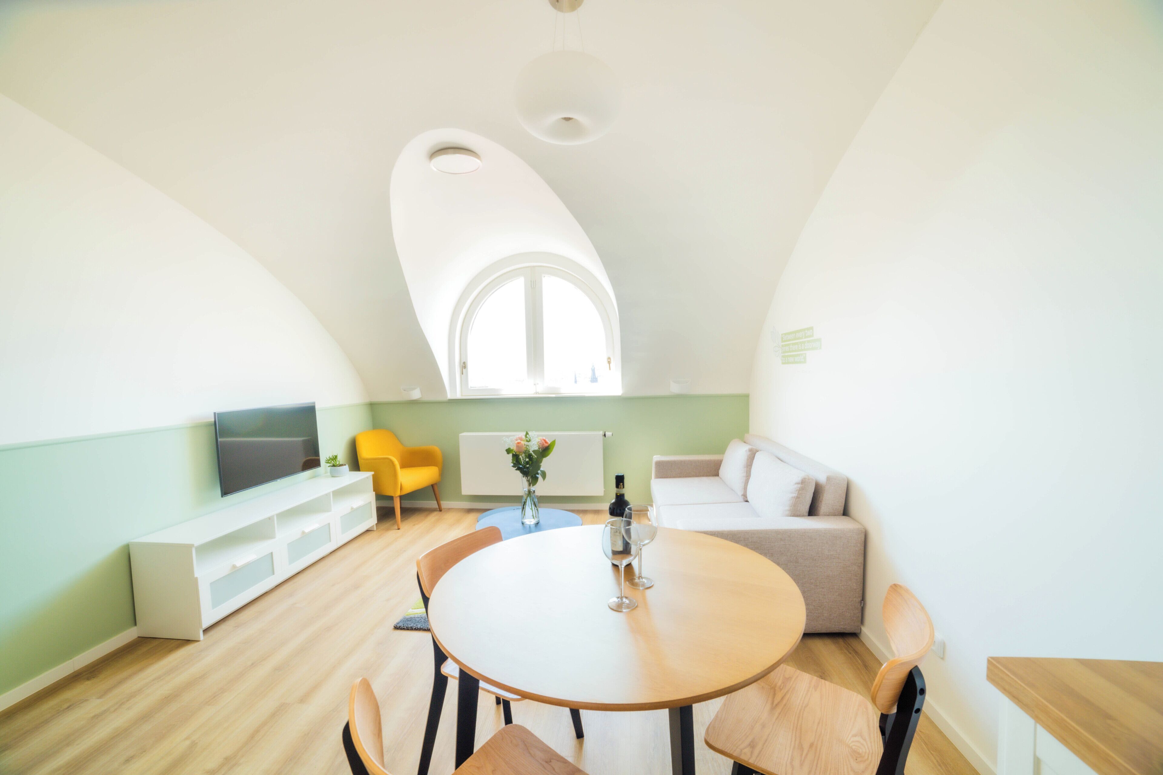 A modern living room with a round dining table, yellow chairs, a sofa, and a TV on a white console.