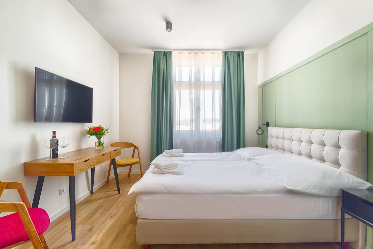 A hotel room with a bed, a desk, a chair, a TV, and a window with curtains.