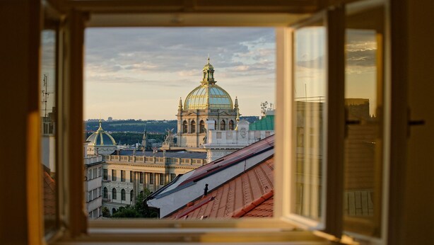 A view through an open window of a historic building with a large dome and classical architecture. - LUMA TERRA PRAGUE (Prague)