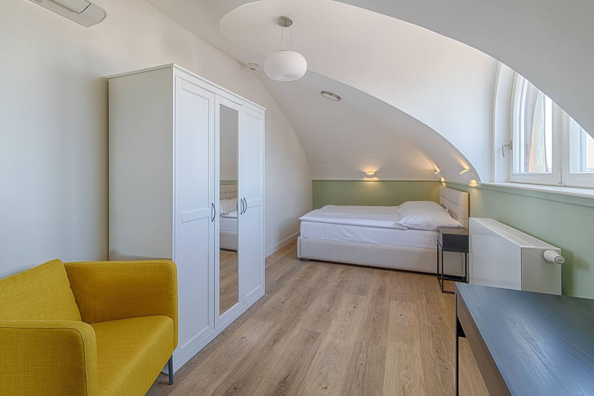 A bedroom with a curved ceiling, a bed, a yellow chair, and a white wardrobe.