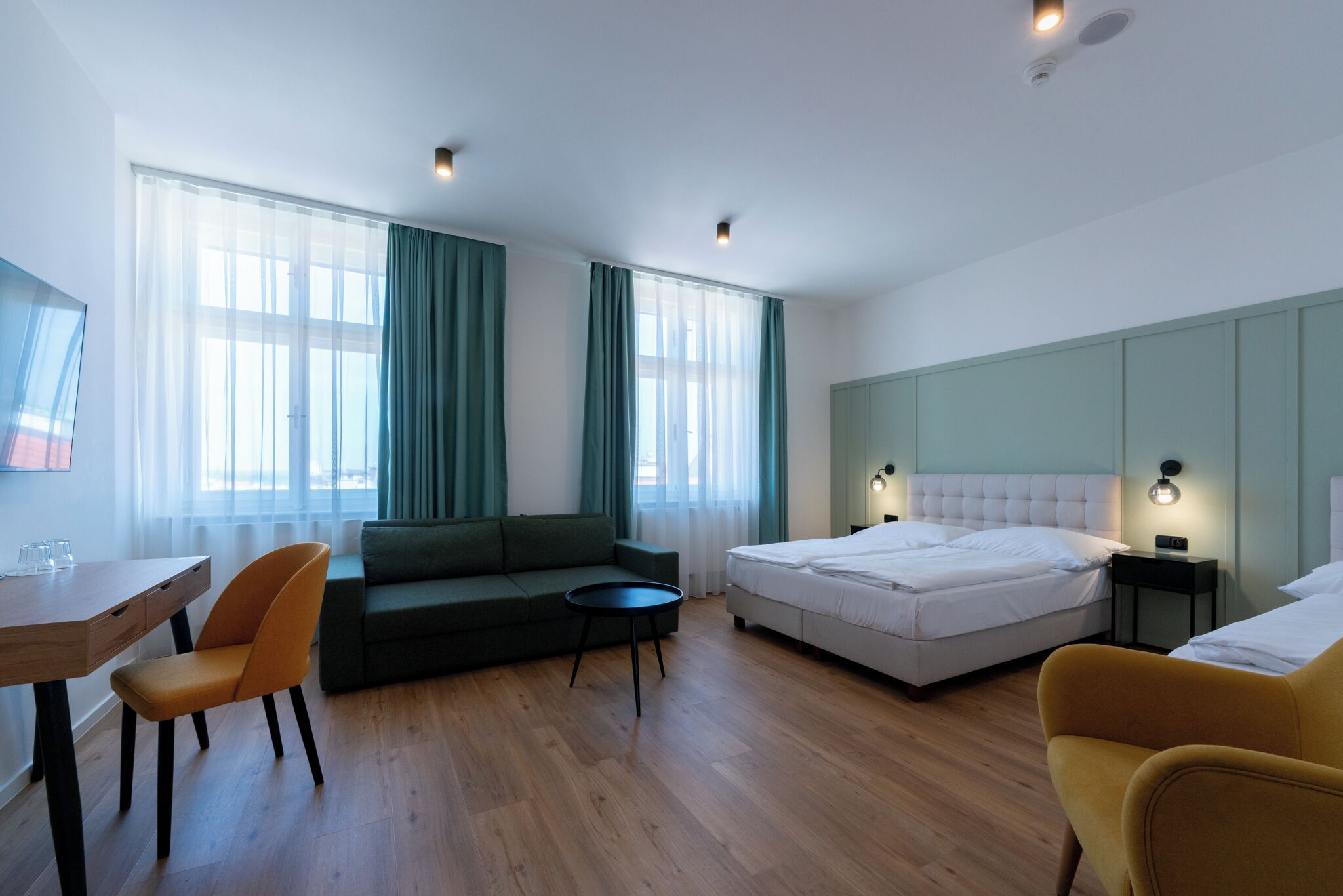 A modern hotel room with a bed, a sofa, a small table, and a desk.