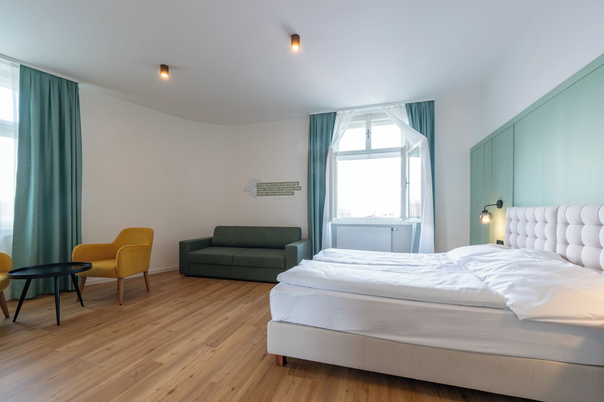 A hotel room with a bed, a sofa, a chair, a small table, and a window with curtains.