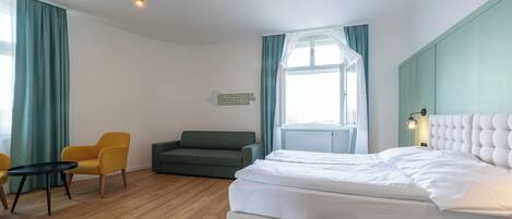 A hotel room with a bed, a sofa, a chair, a small table, and a window with curtains.