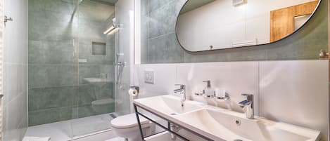 Uma casa de banho moderna com cabine de duche em vidro, sanita, lavatório com espelho e toucador.