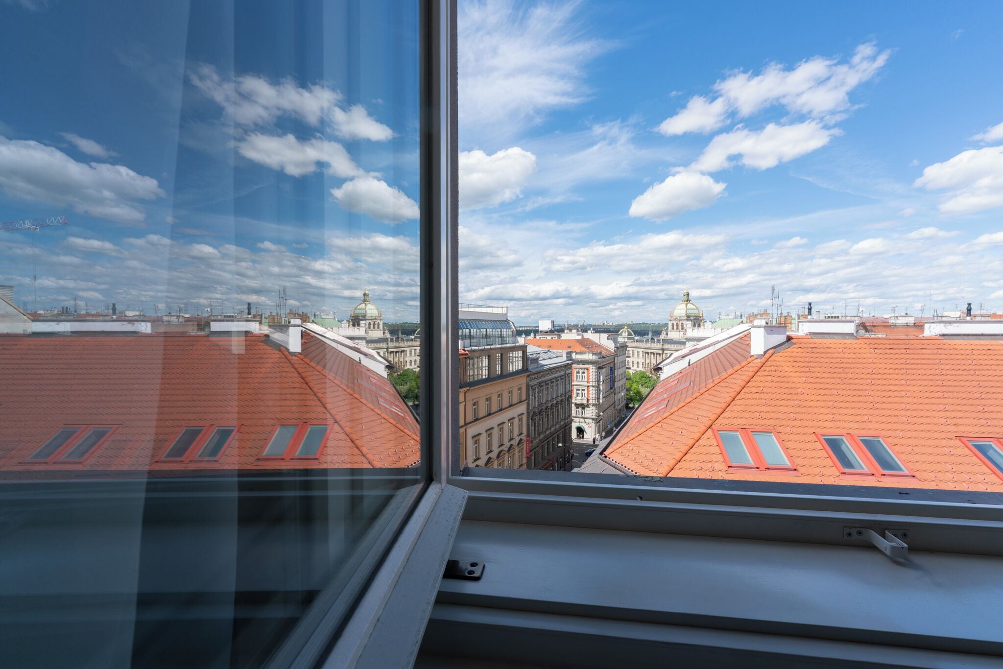 Blick aus einem Fenster auf einen Stadtblick mit roten Dächern und blauem Himmel.