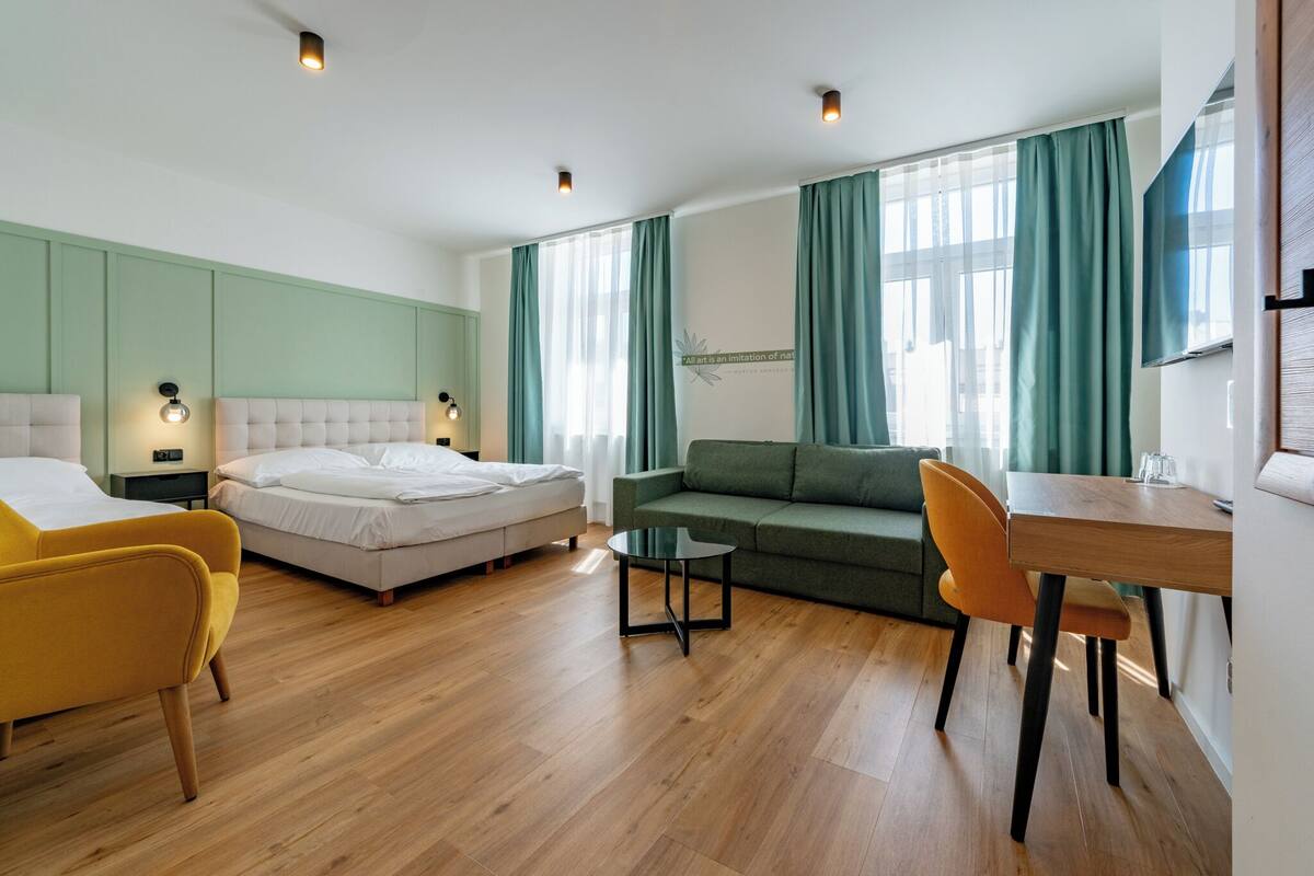 A modern hotel room with a bed, a sofa, a dining table, and a small coffee table.