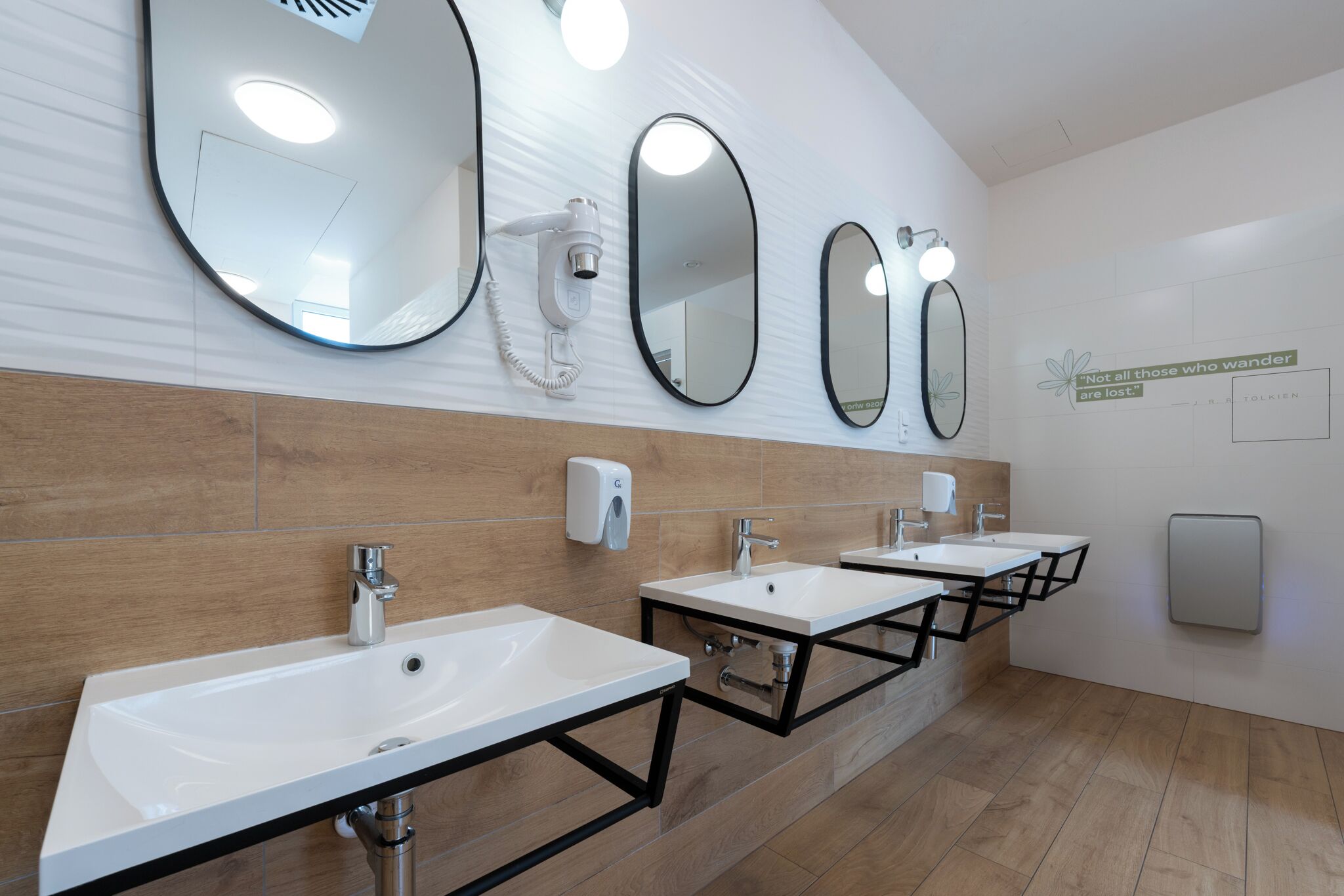 Une salle de bain moderne avec trois lavabos, des miroirs et un sèche-mains.