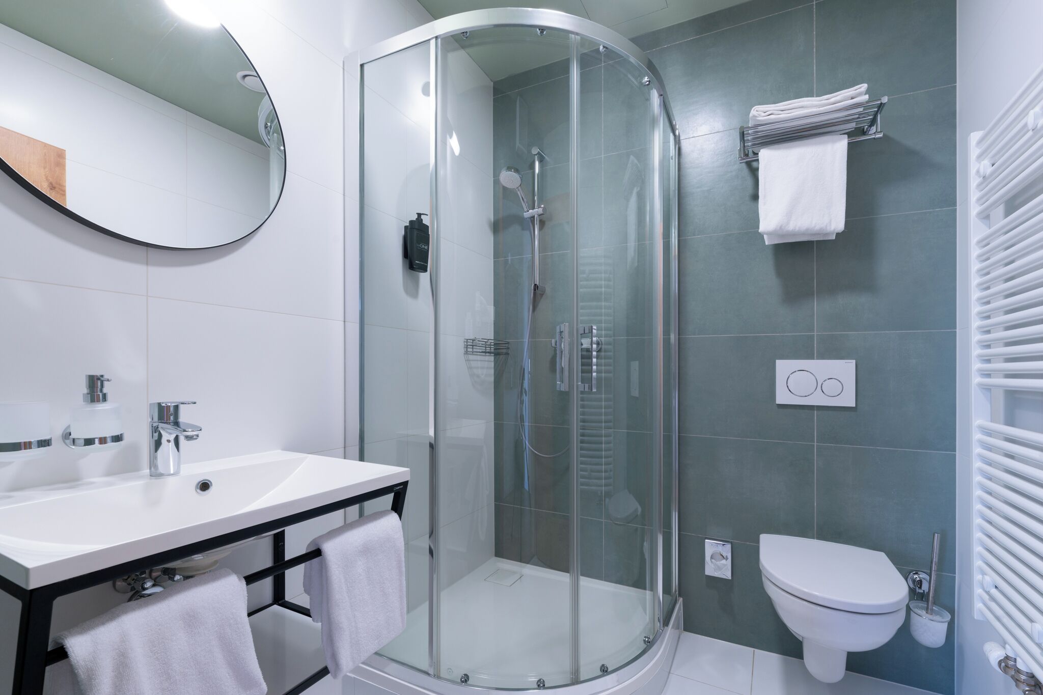 A modern bathroom with a glass-enclosed shower, a white sink with a black frame, and a toilet with a white toilet paper holder.
