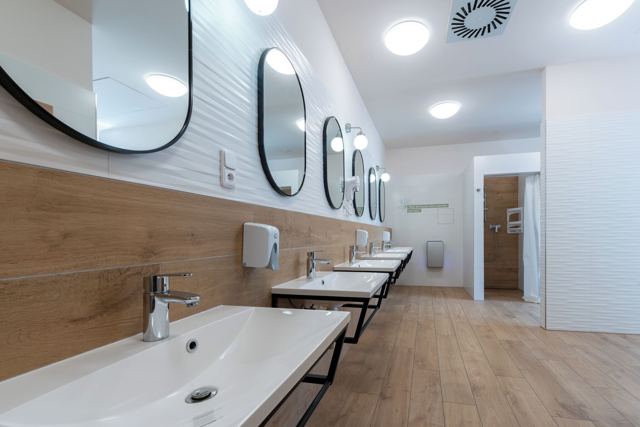 Ein modernes Badezimmer mit mehreren Waschbecken, Spiegeln und automatischen Handtrocknern.