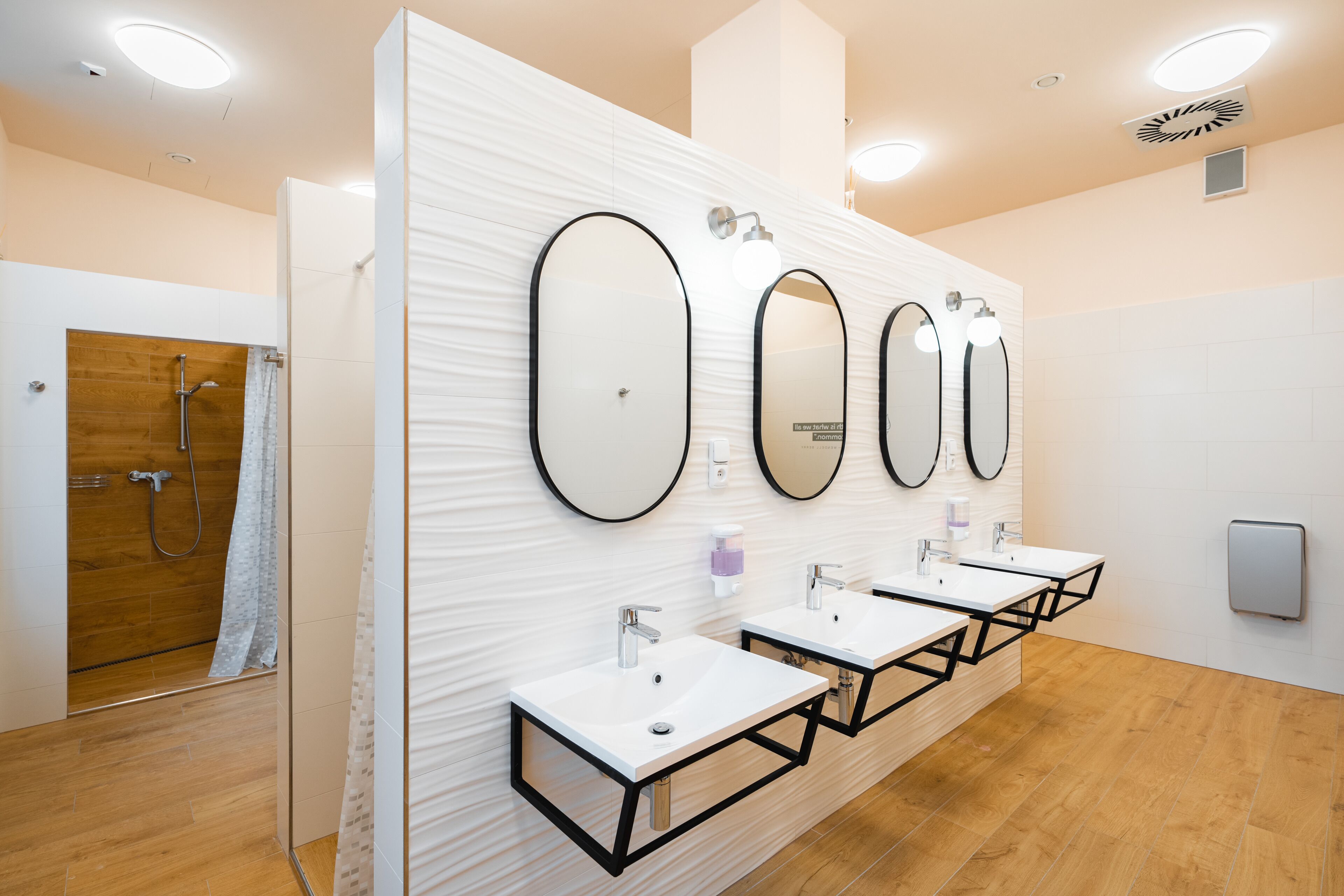 Un baño moderno con tres lavamanos, ducha y pared de espejo.