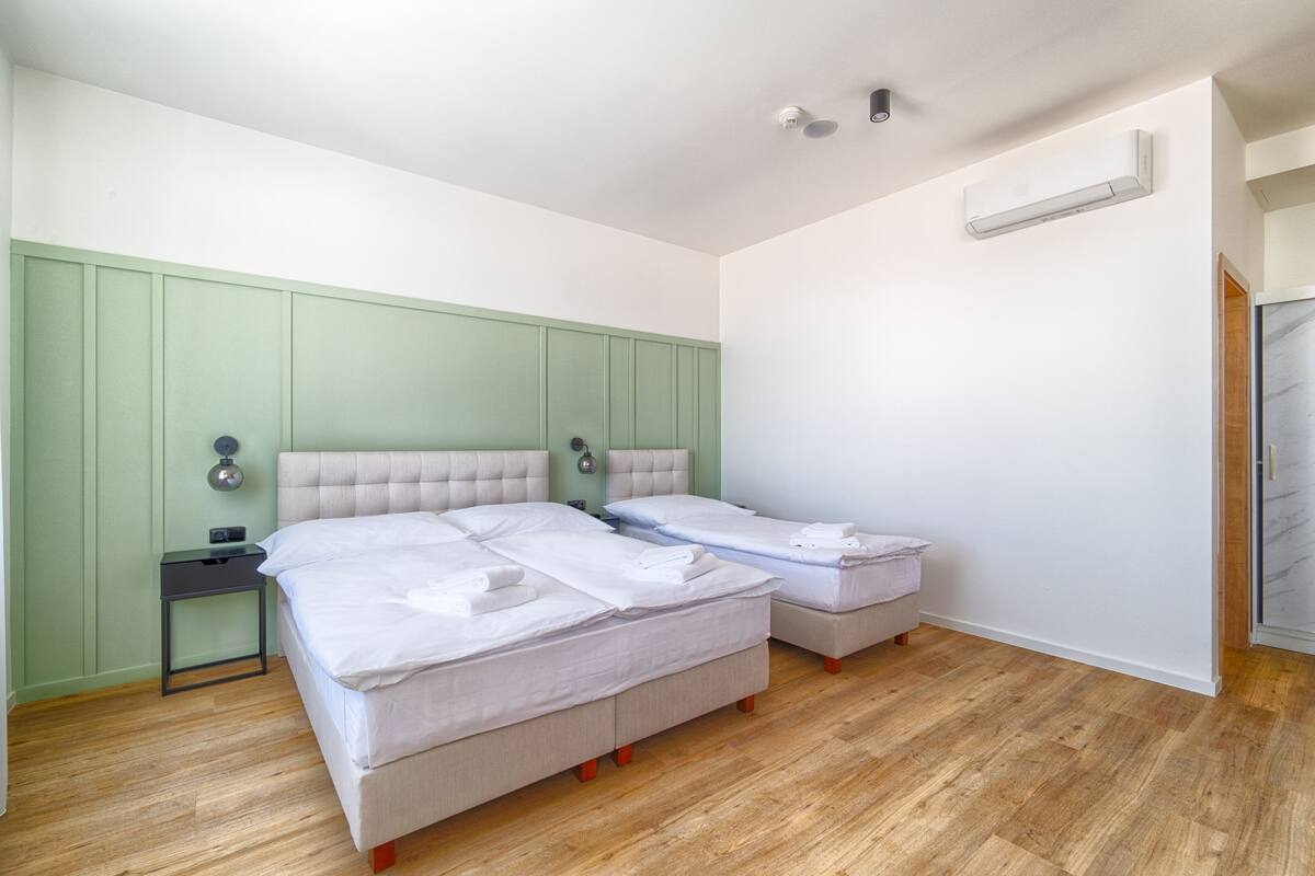 A bedroom with two beds, a nightstand, a wall-mounted air conditioner, and a wooden floor.