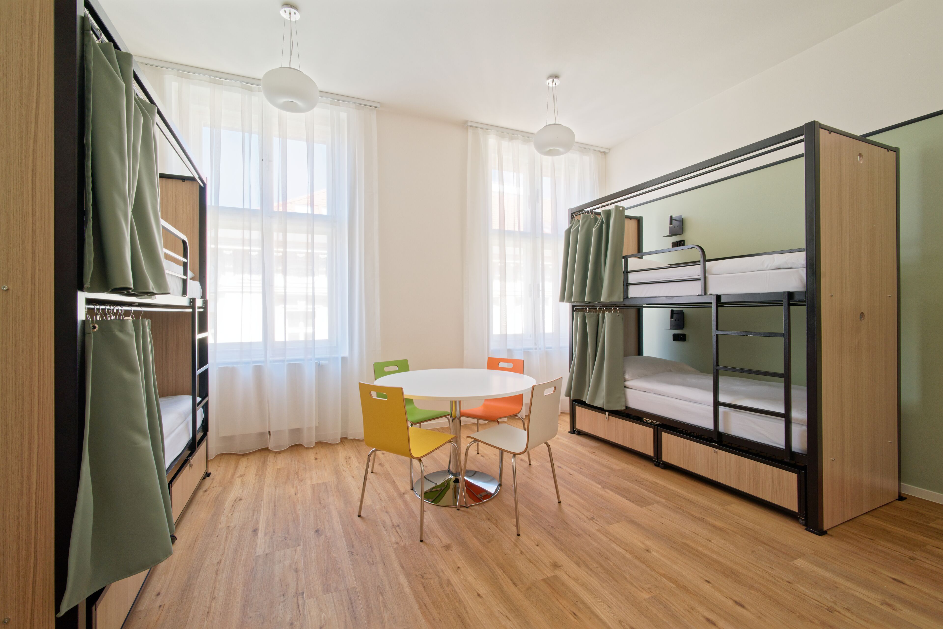 Une petite pièce avec un lit superposé, une petite table avec des chaises et une fenêtre ornée de rideaux légers.