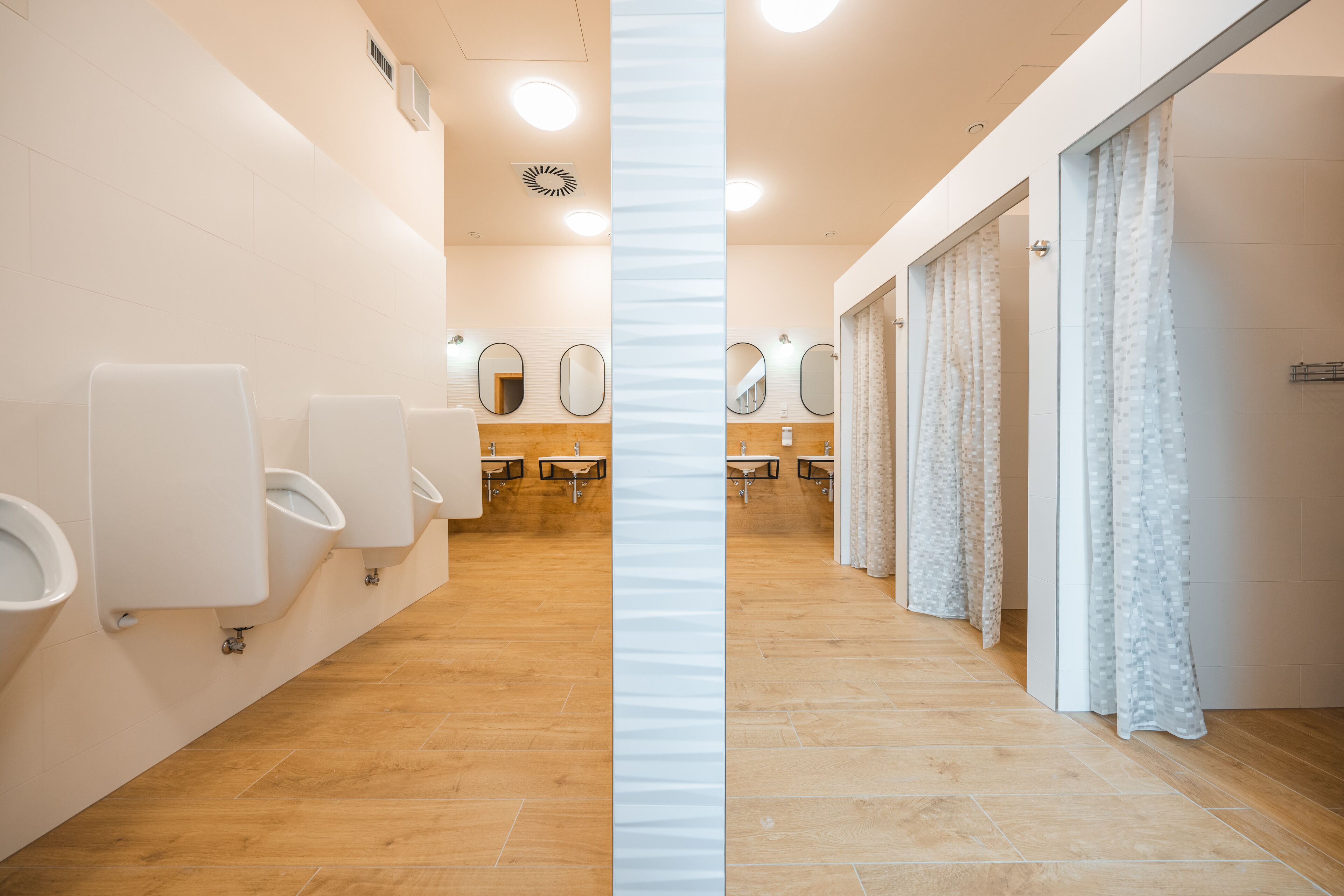 A modern restroom with multiple urinals, mirrors, and a wooden floor.