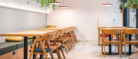 Un comedor moderno con mesas y sillas de madera, piso de mármol y plantas colgantes.