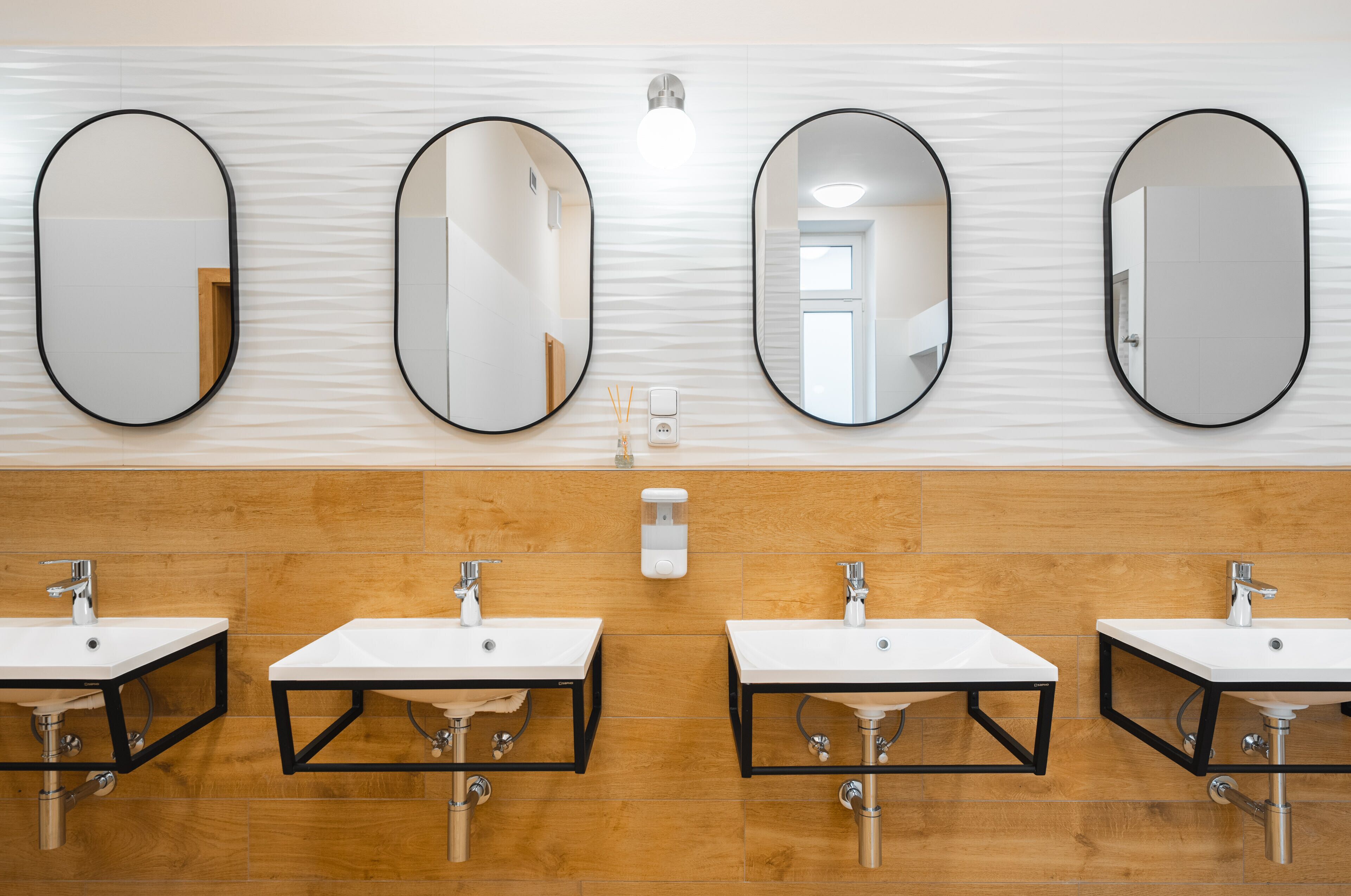 Ein modernes Badezimmer mit drei Waschbecken und drei ovalen Spiegeln.