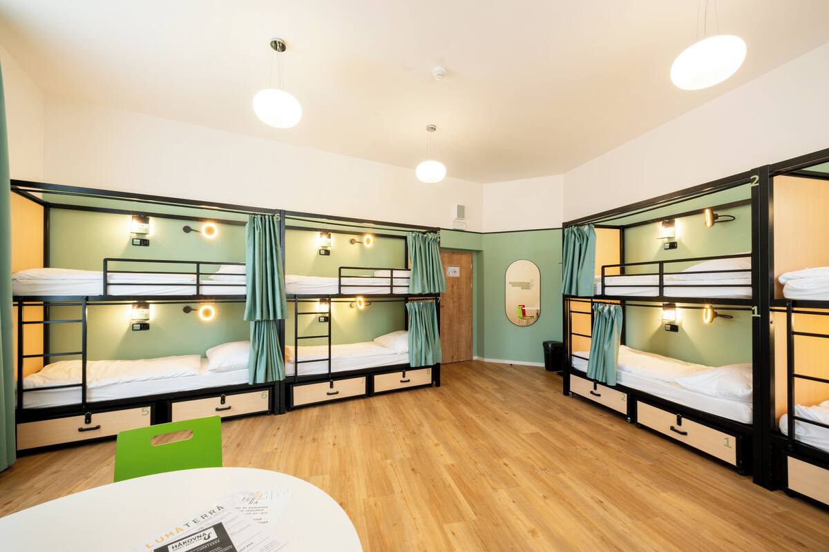 A dormitory room with bunk beds, wooden floors, and a green chair.
