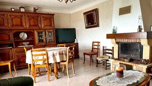 A living room with a fireplace, wooden furniture, a television, and a dining table. - Charming house near AJACCIO (Appietto)