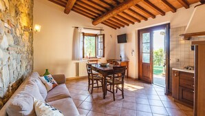 A cozy living room with a wooden ceiling, a stone wall, a sofa, and a dining area with a table and chairs. - Raffaello Apartment ~ LE FRAINE (New Opening 2022) (Santa Luce)