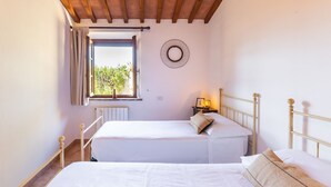 A bedroom with two beds, a wooden ceiling, a window with curtains, a wall clock, and a nightstand with a lamp. - Raffaello Apartment ~ LE FRAINE (New Opening 2022) (Santa Luce)